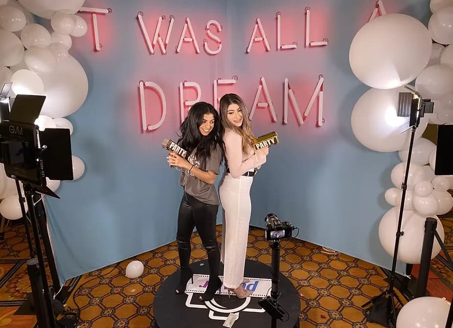 Guests on a 360 photo booth platform in front of an illuminated neon sign