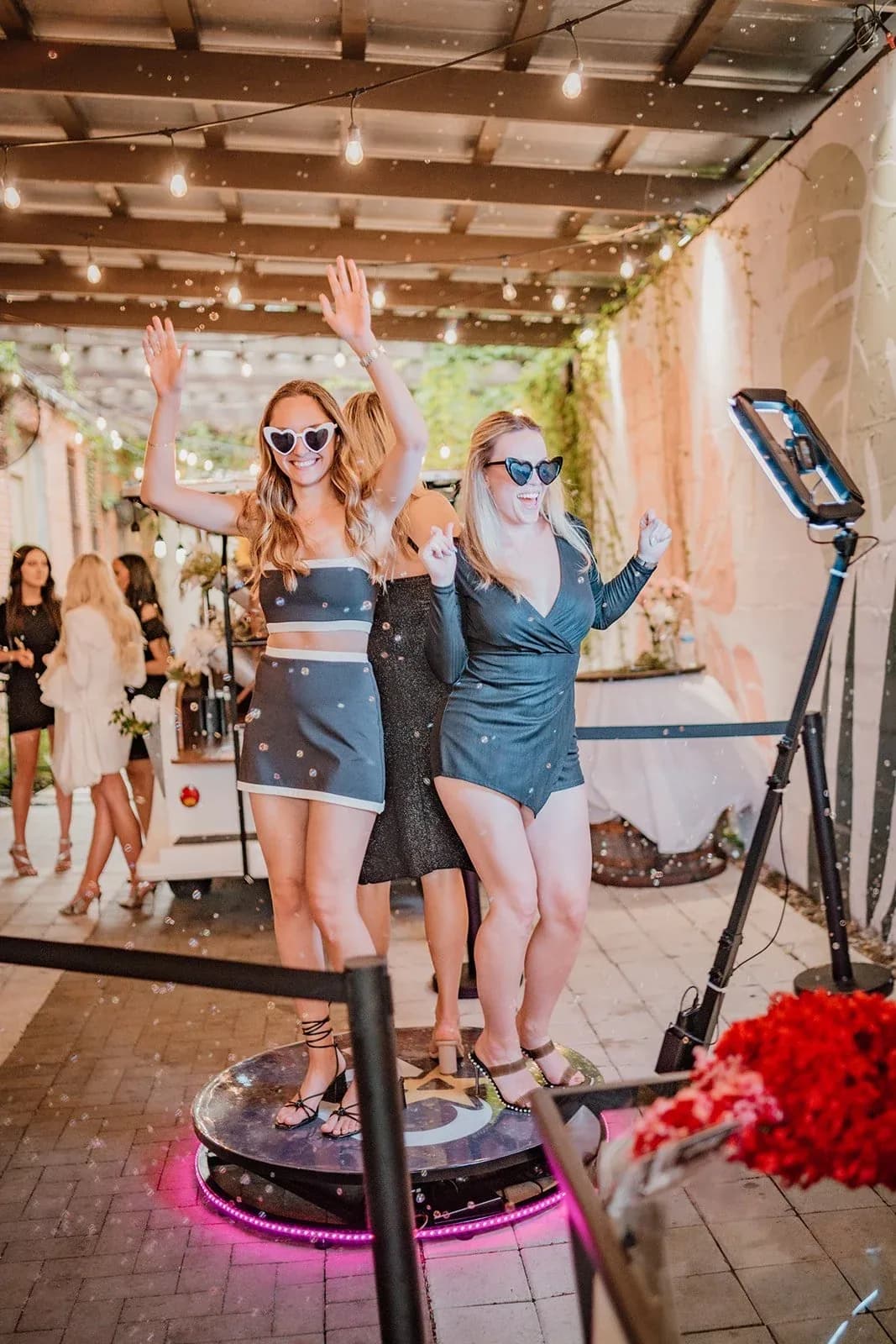 Two wedding guests posing on a 360 video booth platform outdoors
