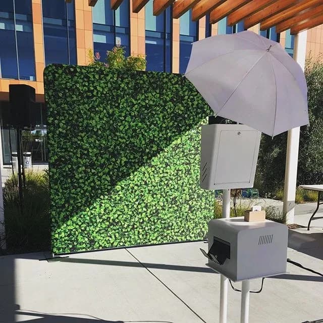 Open air photo booth set up outdoors in front of a greenery hedge wall